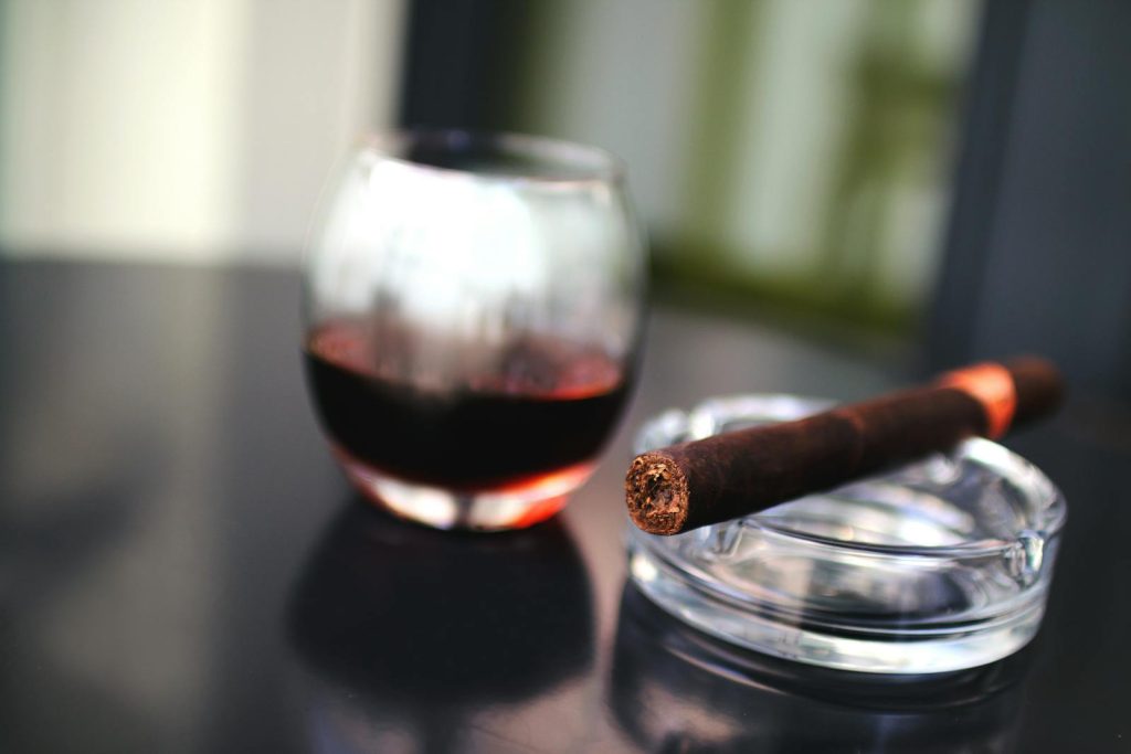 Close-up of a cigar and glass of red wine on a glass table, creating a sophisticated ambiance.